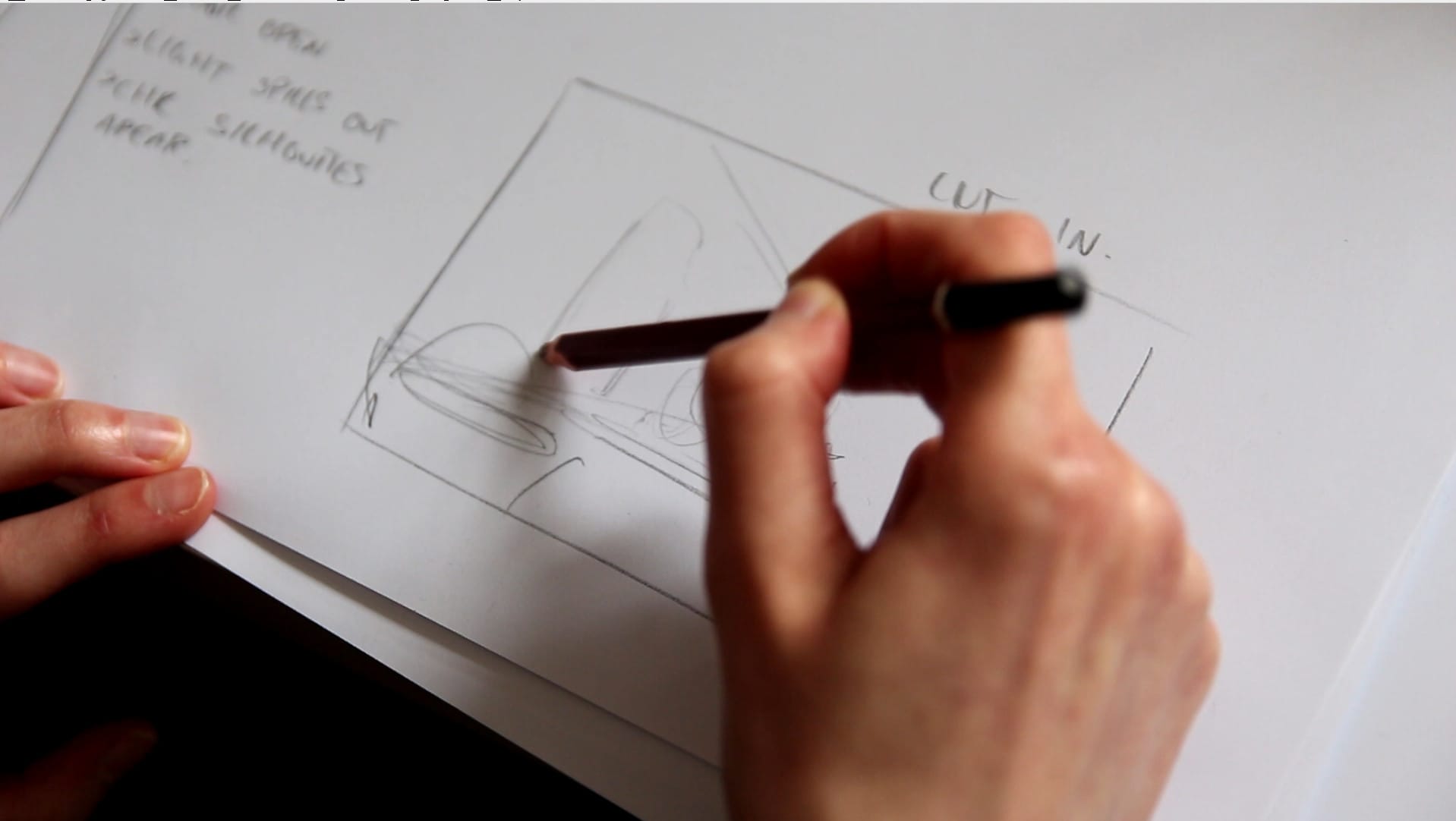 Hand making pencil scene layouts on white paper