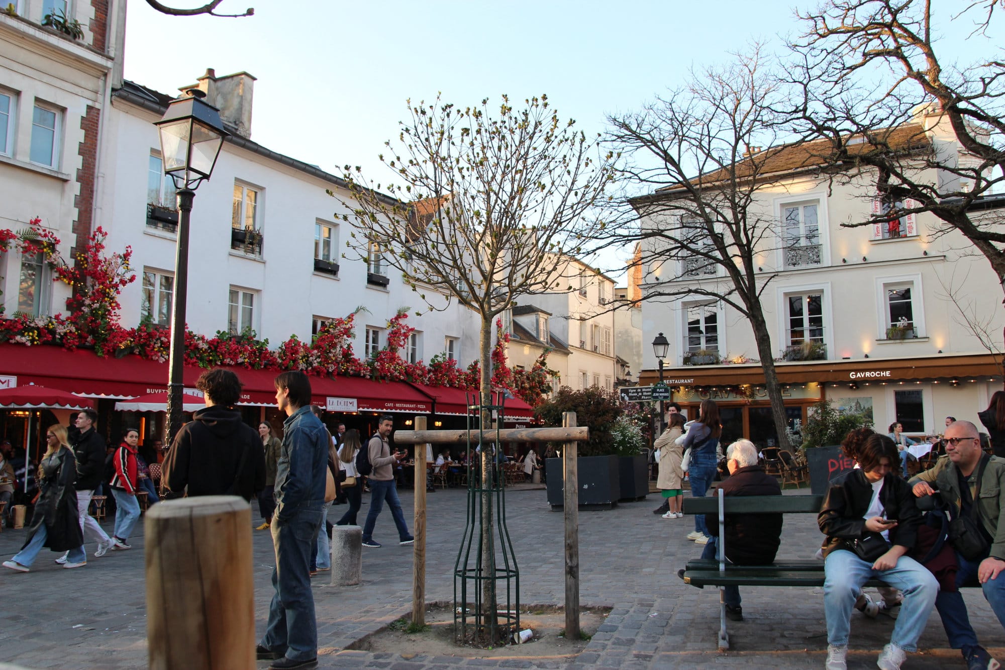 Cobbled town square, with a trees, and white ornate buildings and red awnings