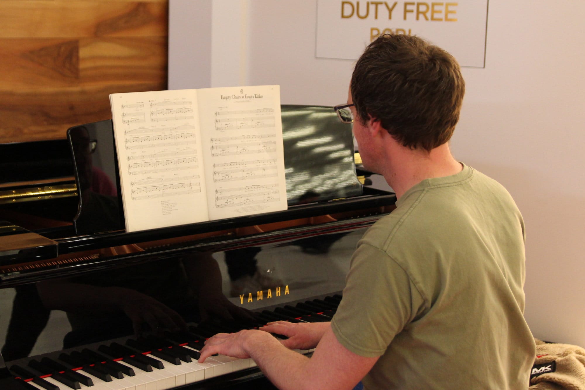 A black piano being played, with the score for 'Empty Chairs at Empty Tables' visible