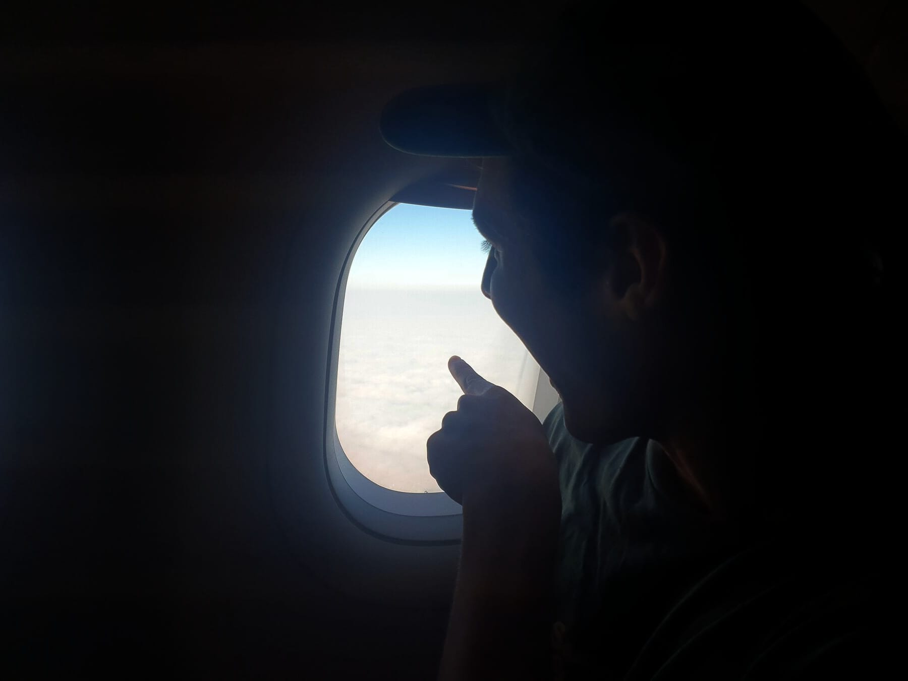 Excited face, pointing out a bight plane window at clouds below